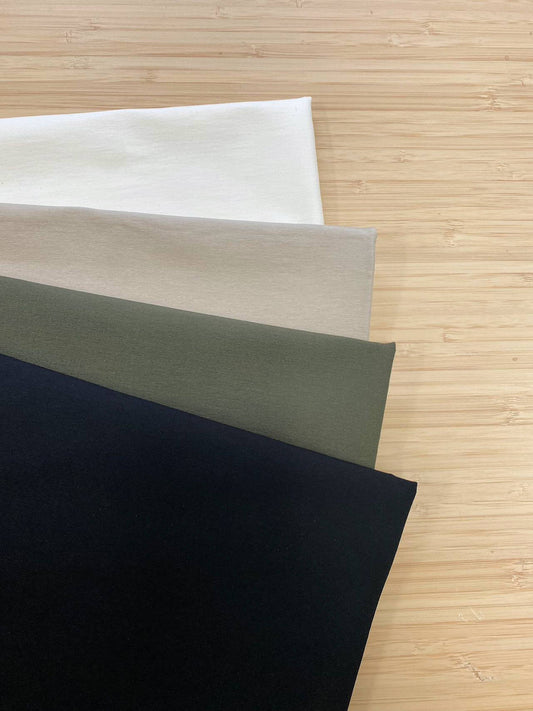 Photo of 4 different colours of 4-Way Stretch Bengaline Fabric  folded and stacked. photographed from above on a wooden table.