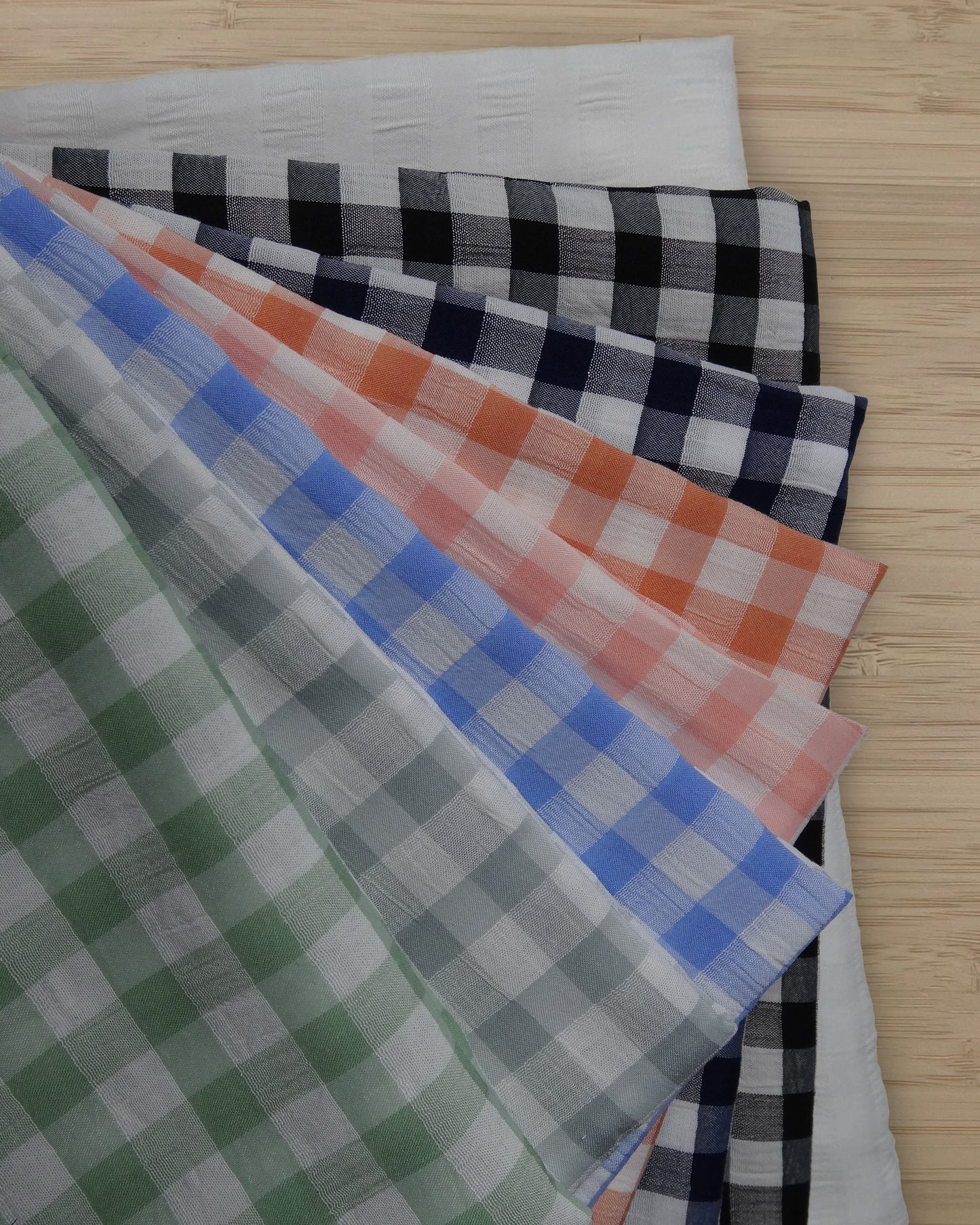 Photo of 6 different colours of check polyester rayon blended fabrics folded and stacked. photographed from above on a wooden table.