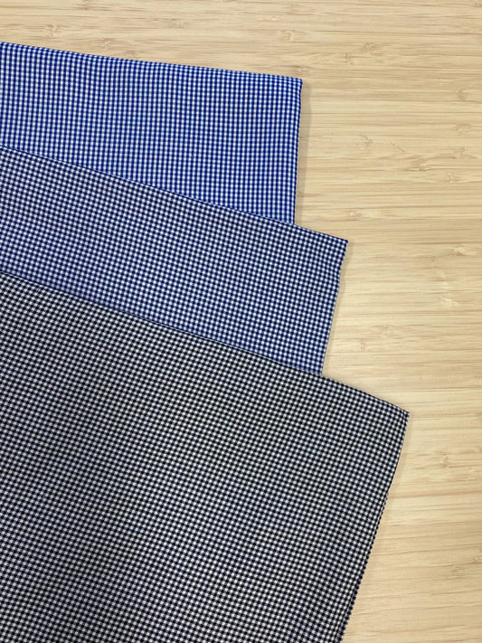 Photo of 3 different colours of Fine Detail Tencel Check fabric folded and stacked. photographed from above on a wooden table.