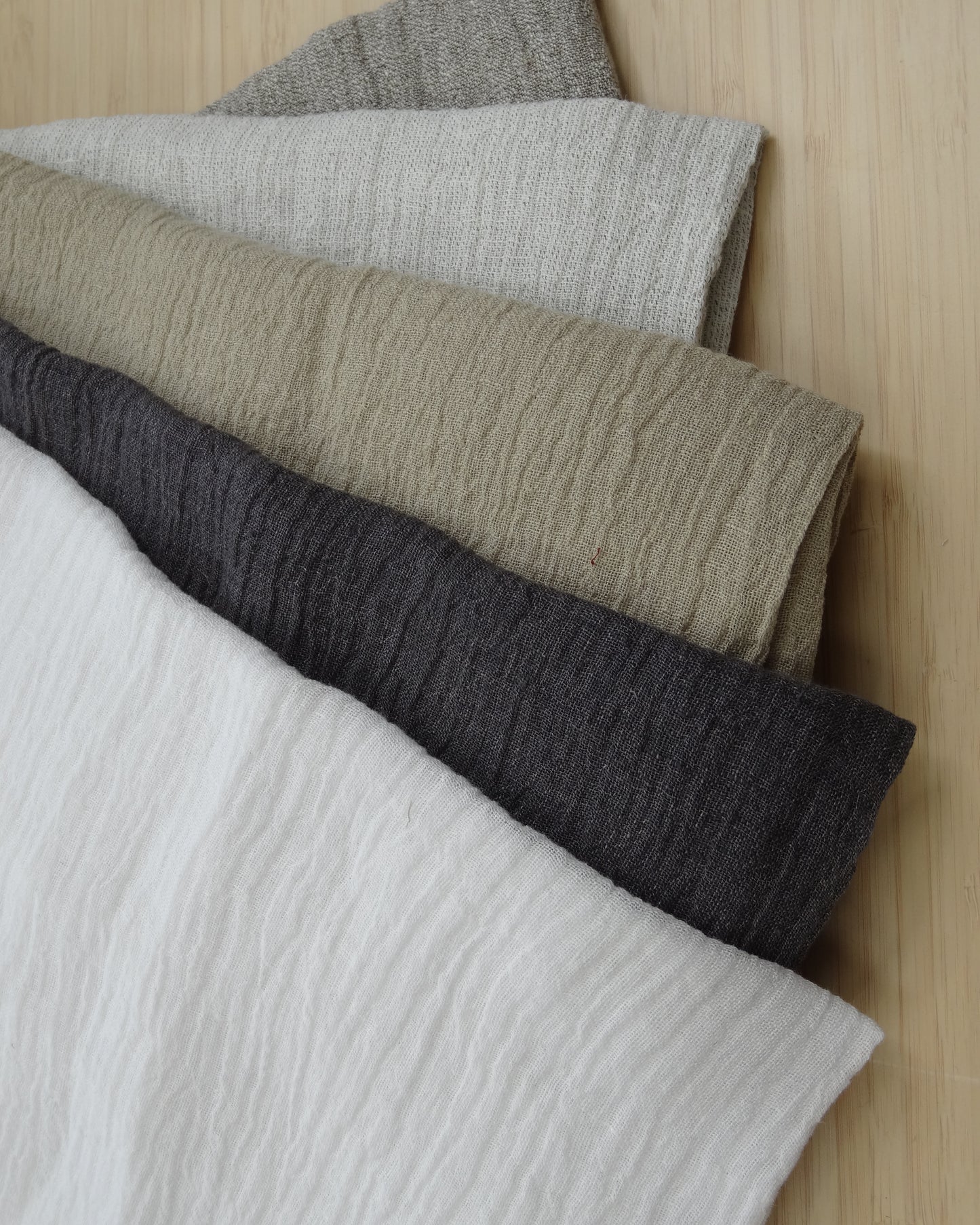 five colous or linen gauze fabric on a wooden table. fabrics in neutral tones