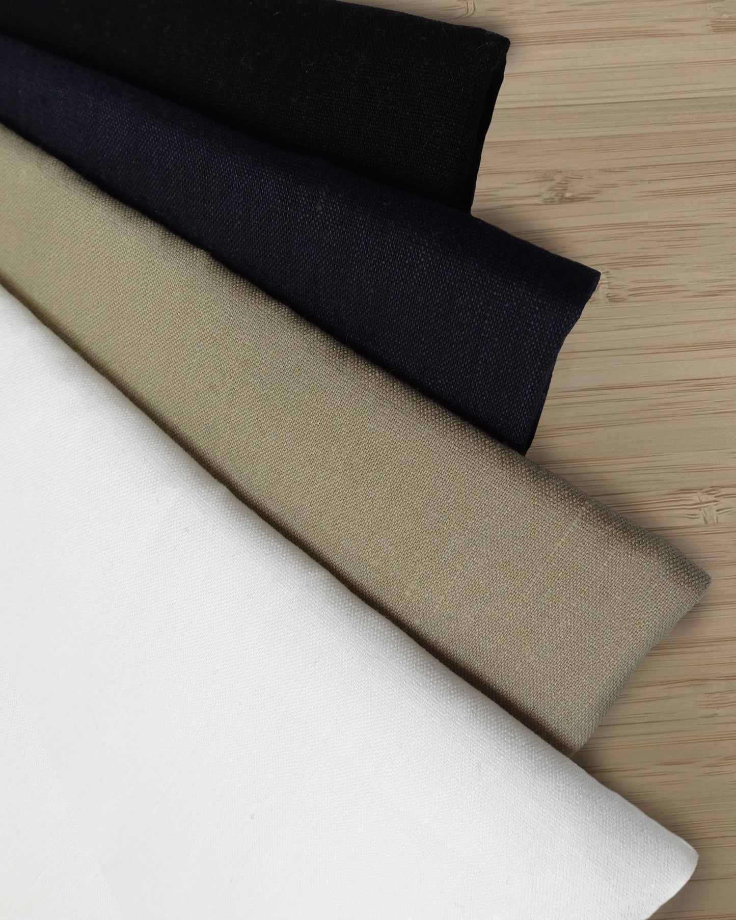 Photo of 4 different colours of linen viscose fabrics folded and stacked.  photographed from above on a wooden table.