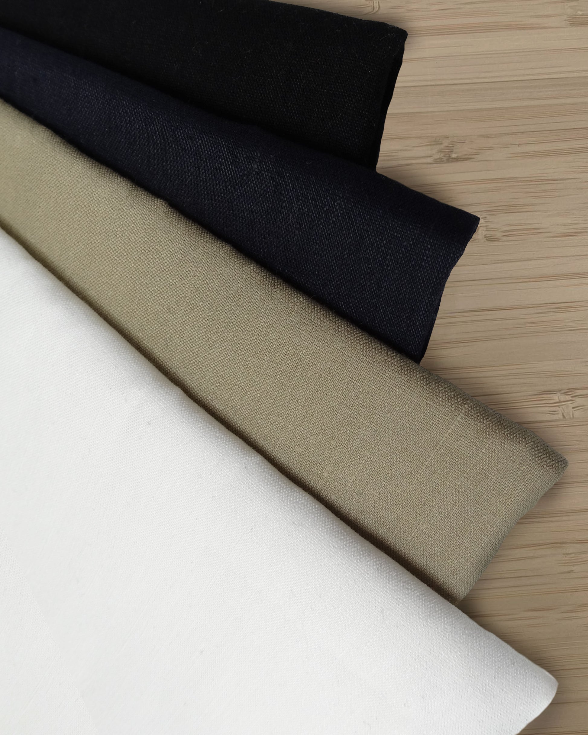 Photo of 4 different colours of linen viscose fabrics folded and stacked.  photographed from above on a wooden table.