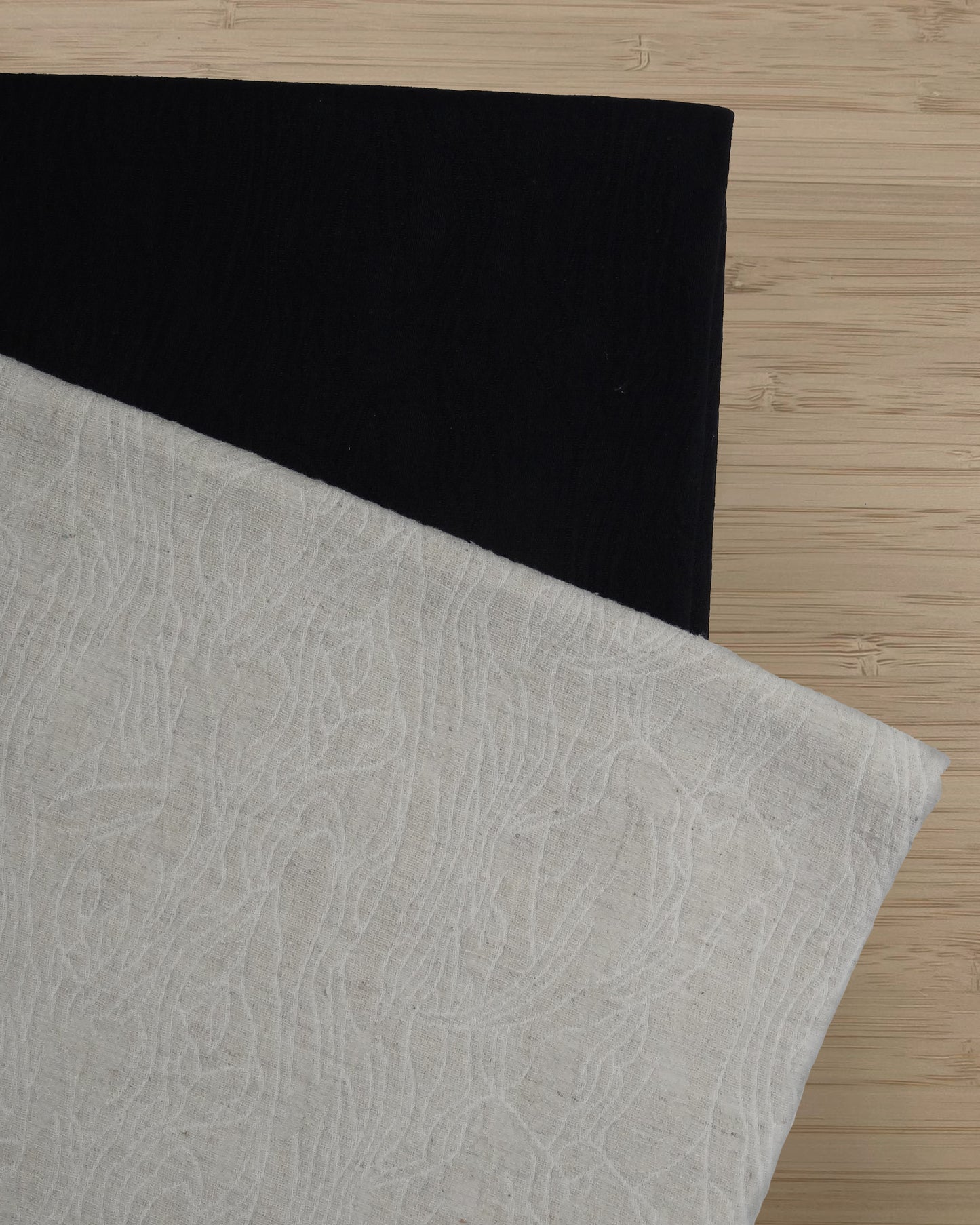 Photo of 2 different colours of linen cotton fabric folded and stacked. photographed from above on a wooden table.