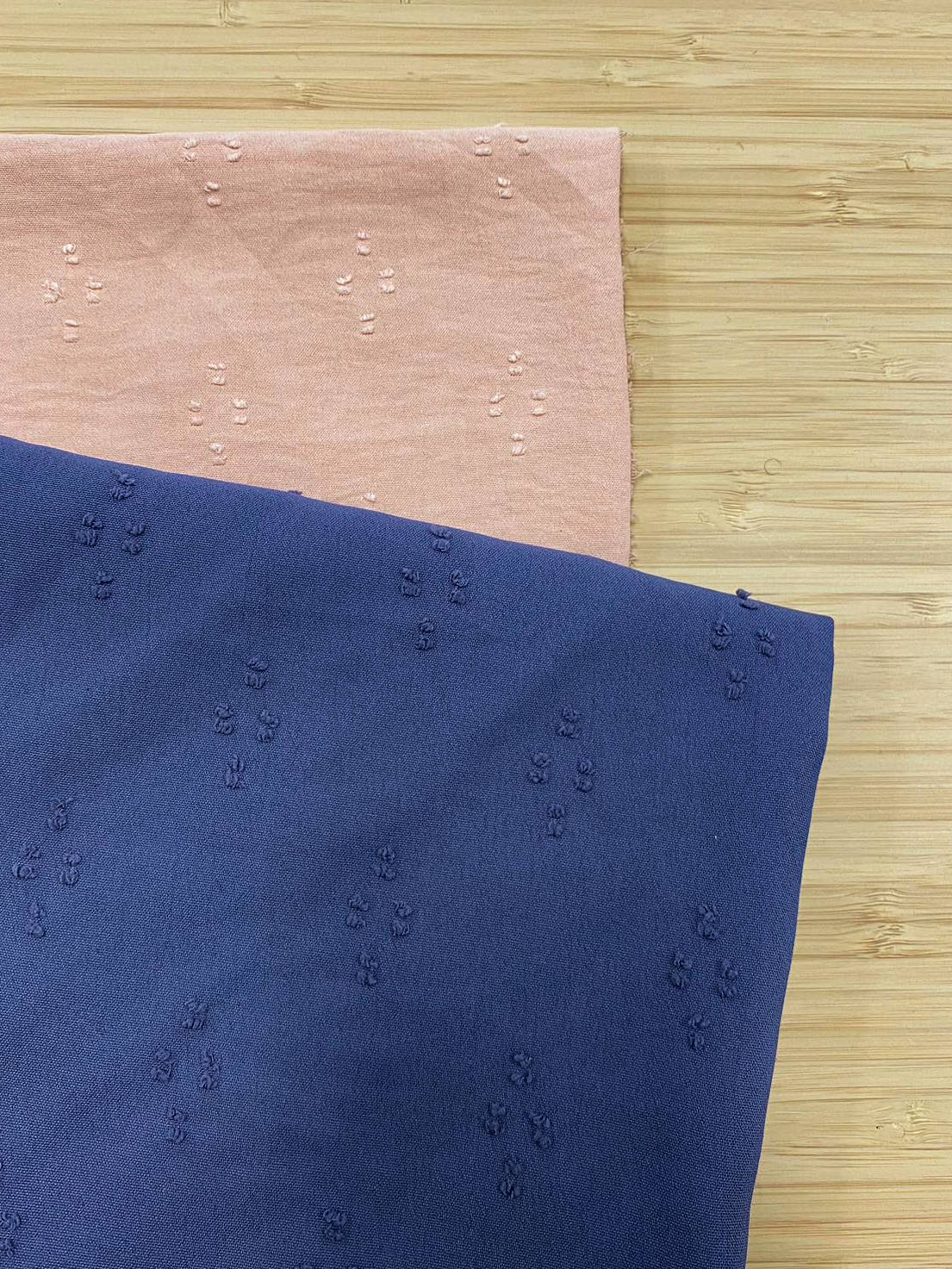 Photo of 2 different colours of Slub Spot detail Jacquard fabric folded and stacked. photographed from above on a wooden table.