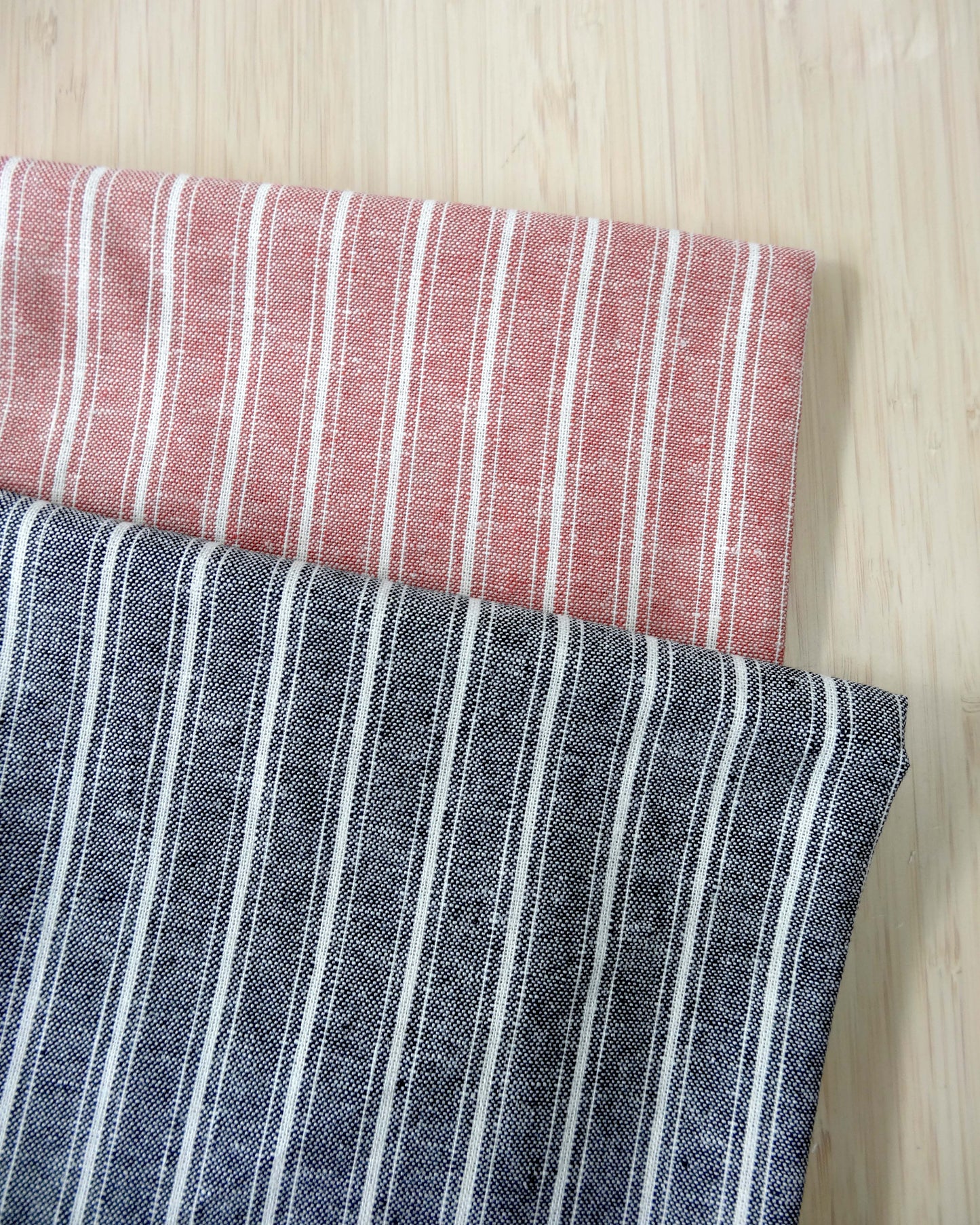 Photo of 2 different colours of striped linen viscose fabrics folded and stacked. photographed from above on a wooden table.