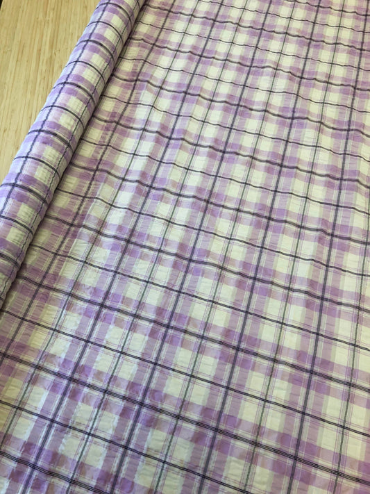 A rolled-up piece of purple checkered fabric with fine black line detailing, lying on a wooden table