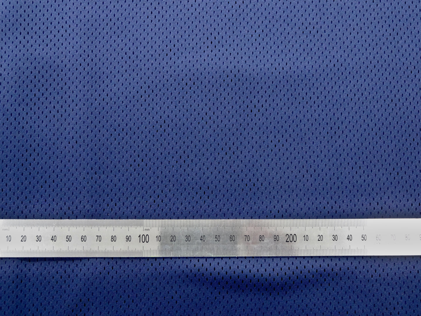 Close up of mesh fabric with metal ruler laid ontop to show spacing and size of the gaps in the mesh