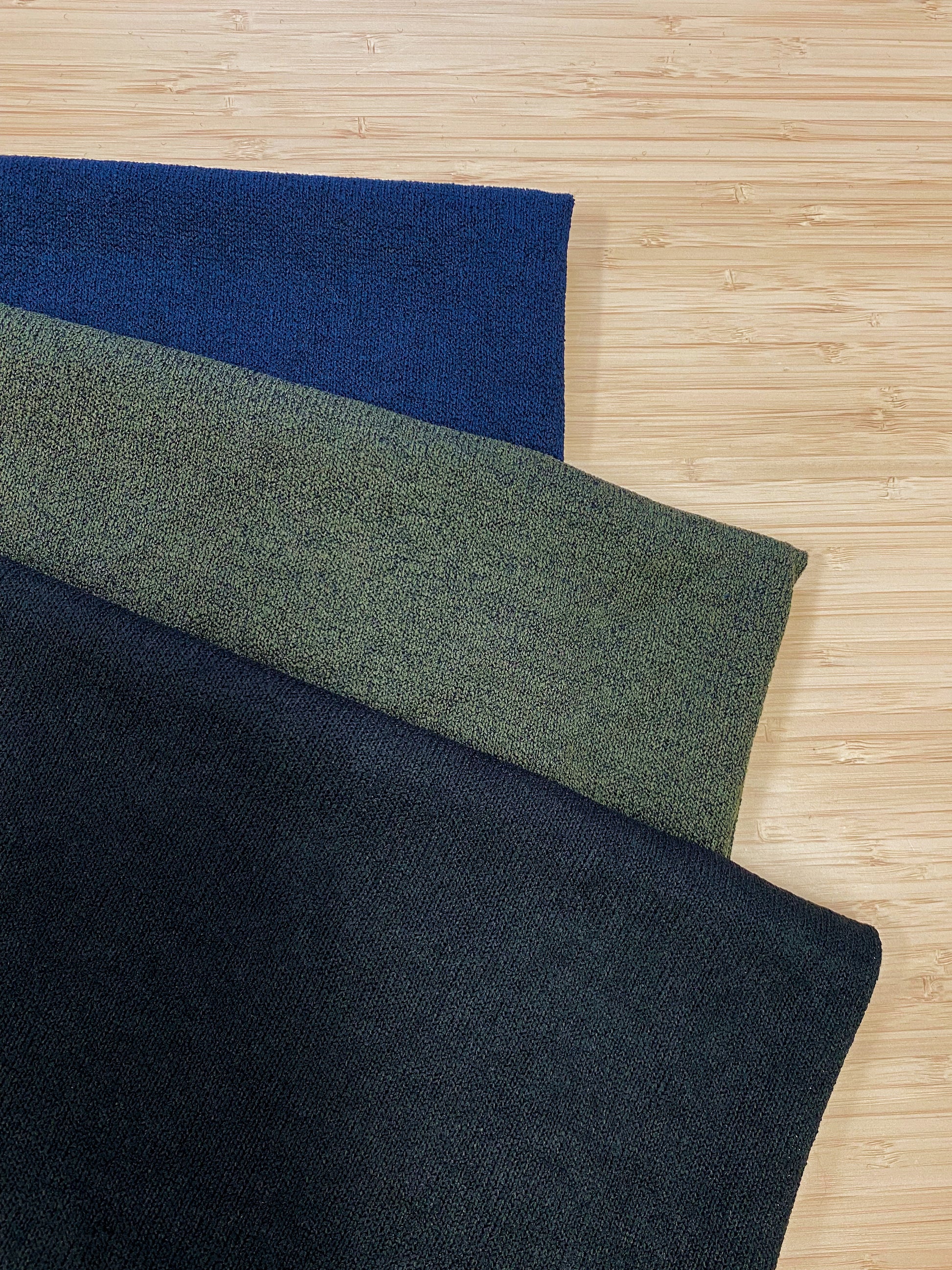 Photo of 3 different colours of  acrylic knitted fabric folded and stacked. photographed from above on a wooden table.