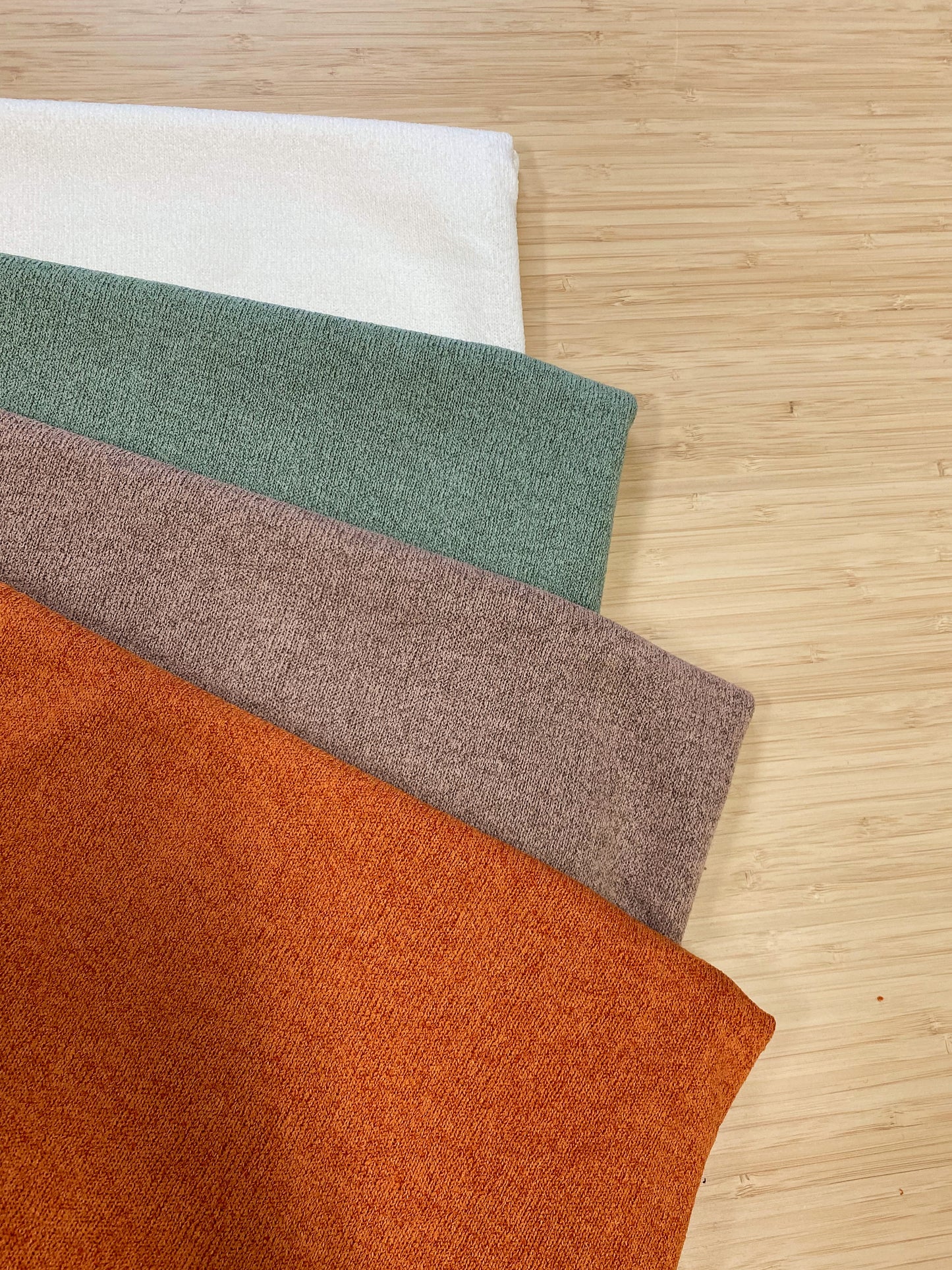 Photo of 4 different colours of  acrylic knitted fabric folded and stacked. photographed from above on a wooden table.