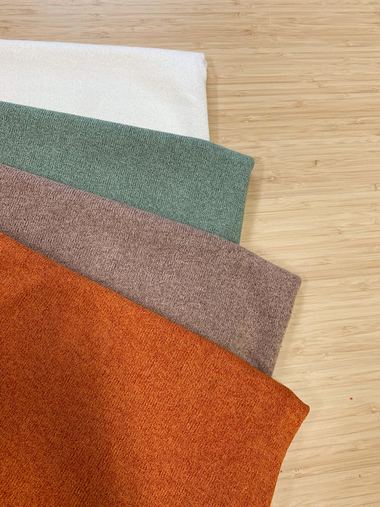 Photo of 4 different colours of  acrylic knitted fabric folded and stacked. photographed from above on a wooden table.