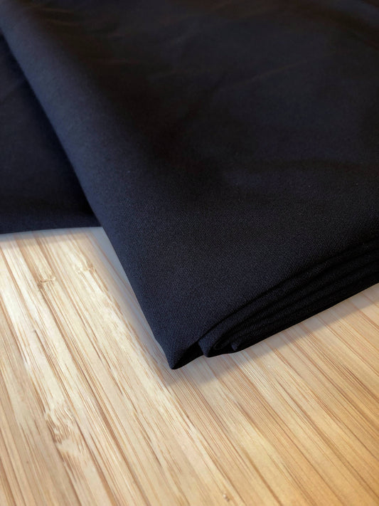 A  black two-way stretch polyester fabric folded and photgraphed on a wooden table