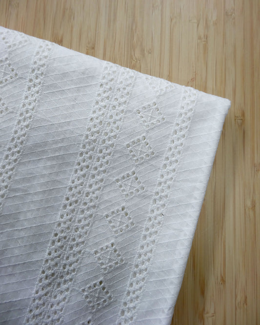 White detailed embroidered cotton fabric folded and photographed from above on a wooden table.