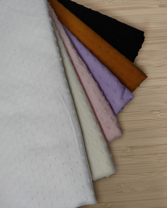 Photo of 6 different colours of cotton spotted slub fabrics folded and stacked.  photographed from above on a wooden table.