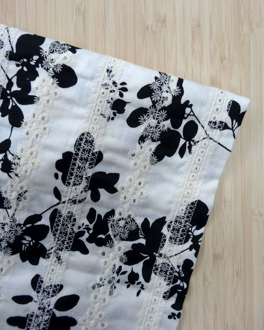 Close-up of a black floral print on white fabric with embroidered line details photographed from above on a wooden table 