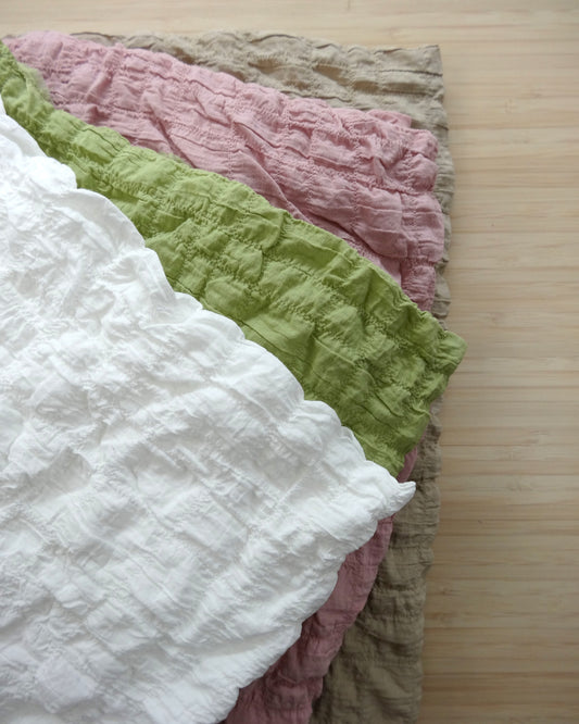 Photo of a gathered cotton spandex fabric in white, green, pink, and fawn on a wooden table. photographed from above.