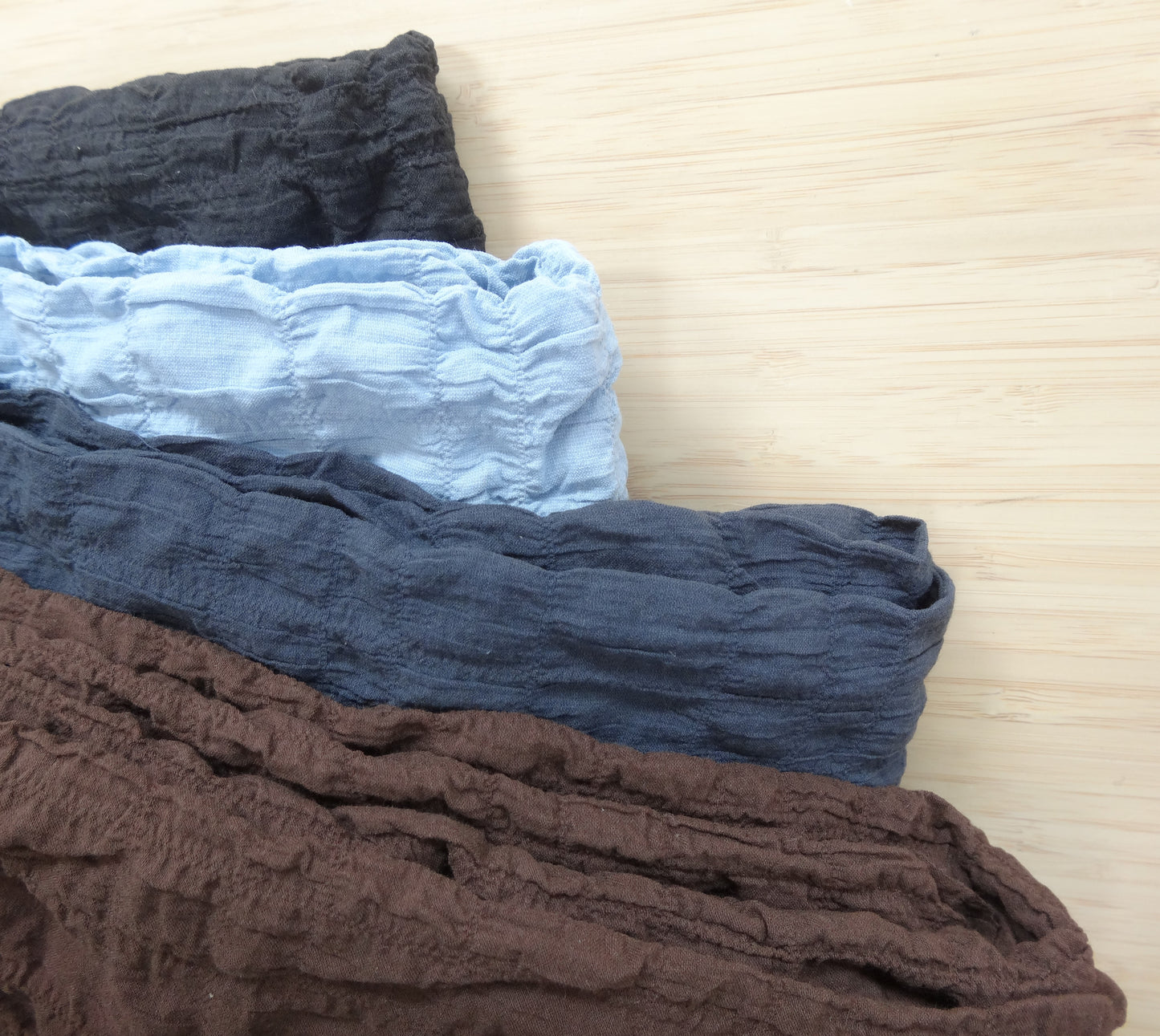 Photo of a gathered cotton spandex fabric in brown, grey, blue, and black on a wooden table. photographed from above.