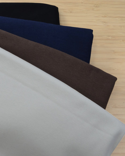 Four colours of a heavy cotton knit fabric pack folded and stacked on a wooden table