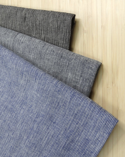 three colours of herringbone fabric remnants folded and stacked on a wooden table