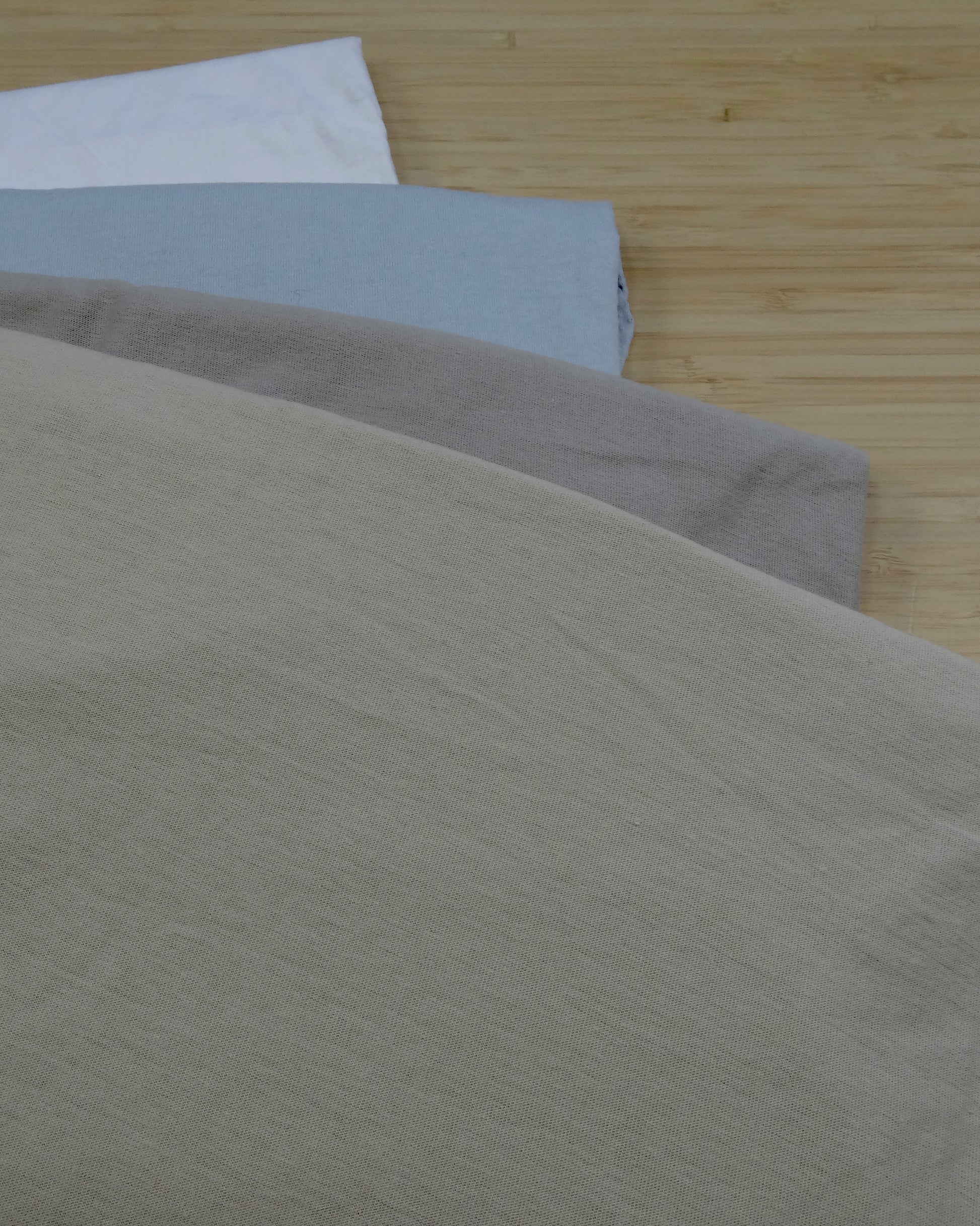 Four light colours of jersey knitted remnant fabrics, folded and stacked on a wooden table