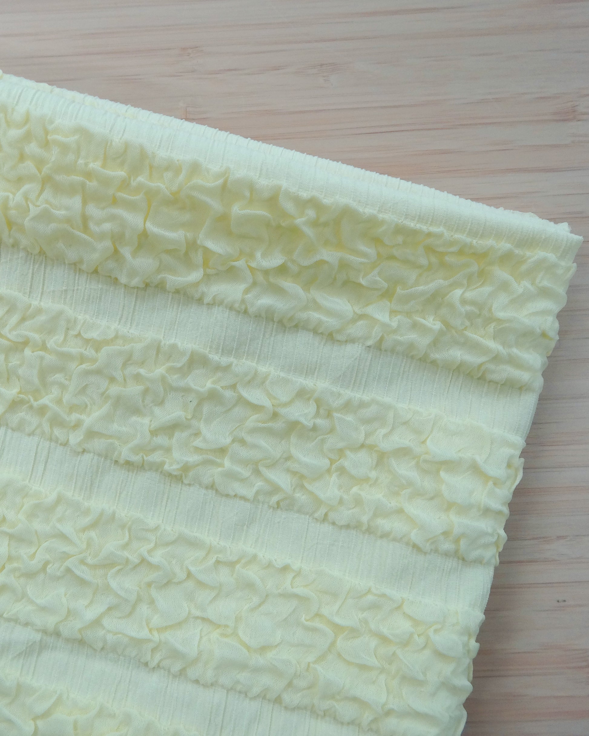 Photo of a Banded Ruffle knit in Yellow on a wooden table. photographed from above.
