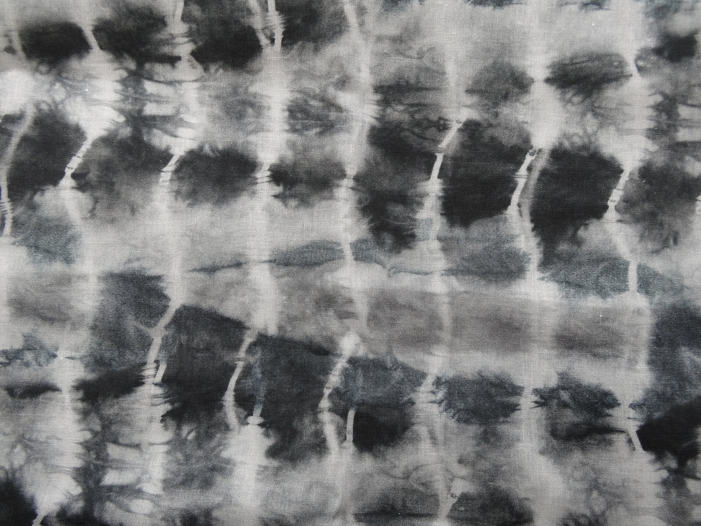 Photo of ripple design printed linen cotton blended fabric remnant in black/greys  on a wooden table. photographed from above.