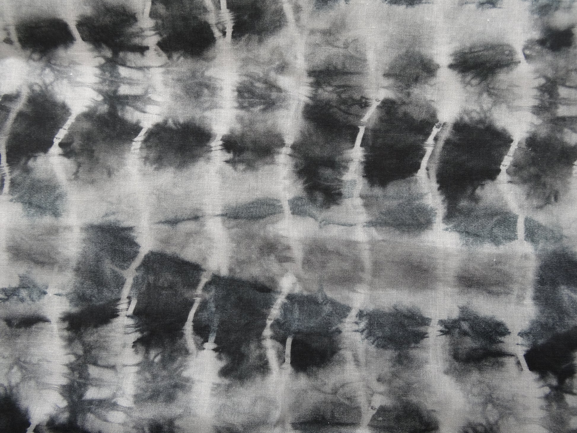 Photo of ripple design printed linen cotton blended fabric remnant in black/greys  on a wooden table. photographed from above.