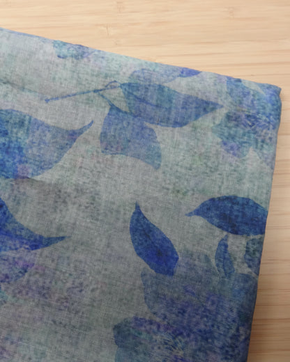 Photo of leafy floral digital print on lightweight ramie fabric remnants stacked in blue on a wooden table. photographed from above.