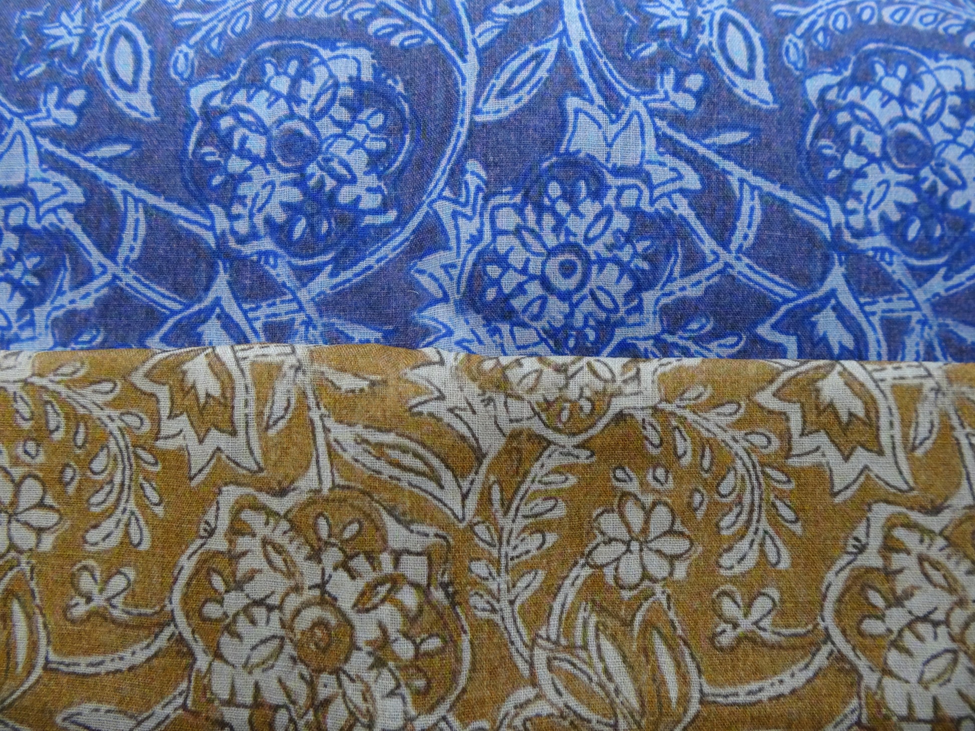 Photo of drawn floral digital print on lightweight ramie fabric remnants stacked in blue and mustard. photographed from above.