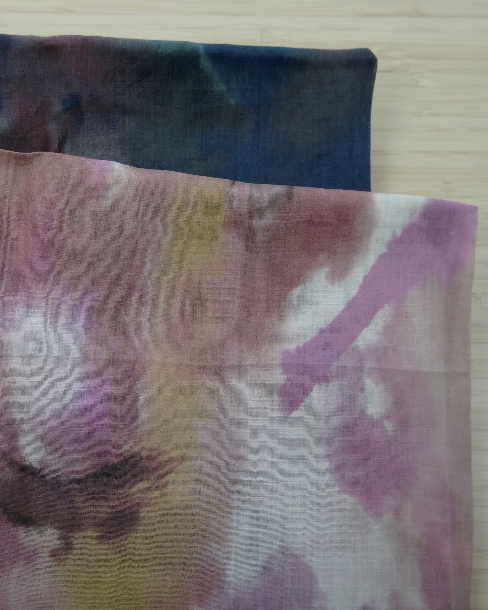 Photo of abstract digital print on lightweight ramie fabric remnants stacked in pinks and navy blues on a wooden table. photographed from above.