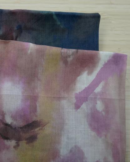 Photo of abstract digital print on lightweight ramie fabric remnants stacked in pinks and navy blues on a wooden table. photographed from above.