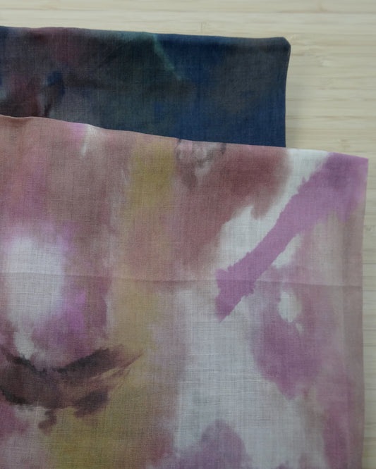 Photo of abstract digital print on lightweight ramie fabric remnants stacked in pinks and navy blues on a wooden table. photographed from above.
