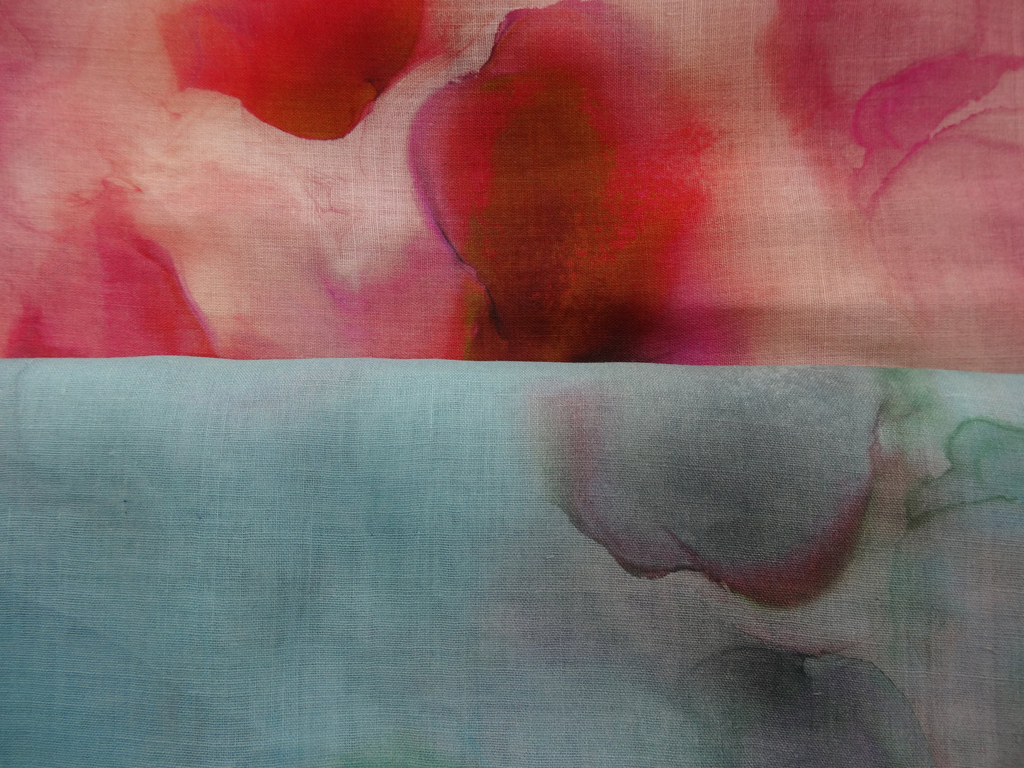 Photo of abstract watercolour abstract digital print on lightweight ramie fabric remnants stacked in blues and pinks. photographed from above.