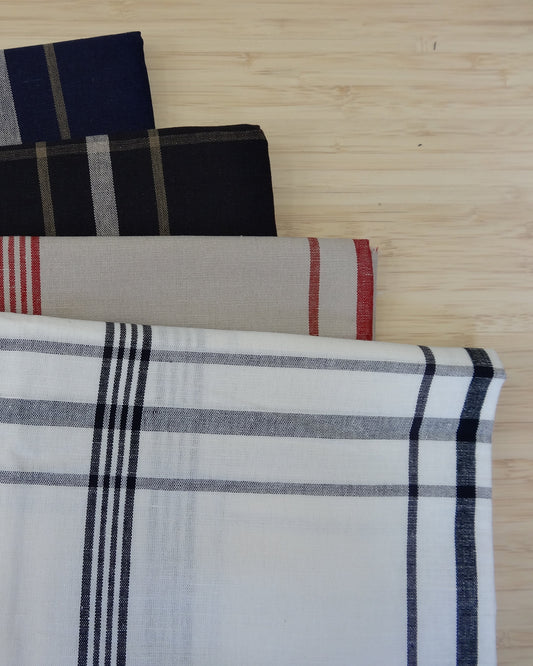 Photo of 4 different colours of checked linen cotton fabric folded and stacked.  photographed from above on a wooden table.