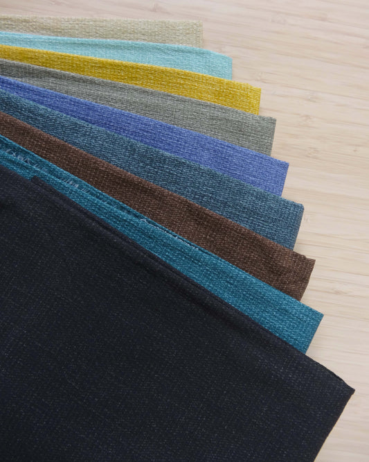 Photo of 9 different colours of pigment printed fabrics folded and stacked and photographed from above on a wooden table.