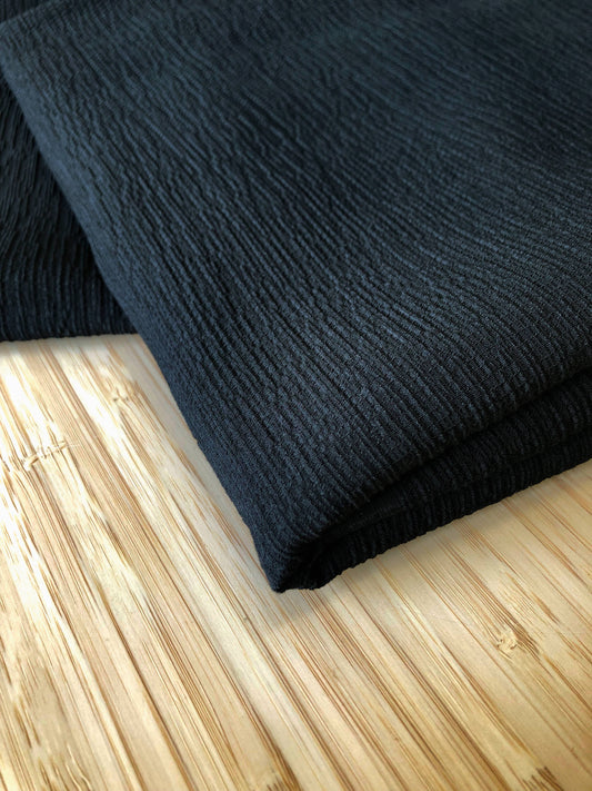 Photograph of Black shirred fabric folded and presented on a wooden table.