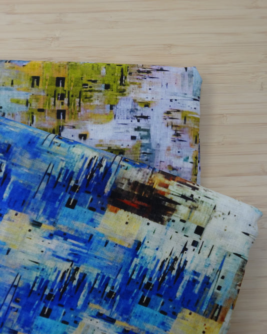 Photo of abstract  shapes printed on linen cotton blended fabric remnants stacked in yellow/greens and bluesColours on a wooden table. photographed from above.