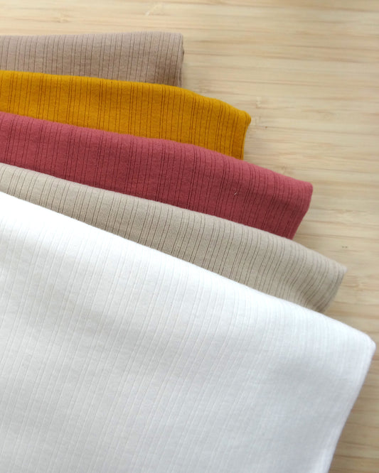 
Photo of a stetchy mesh fabric in white, latte, pink, mustard, and fawn on a wooden table. photographed from above.