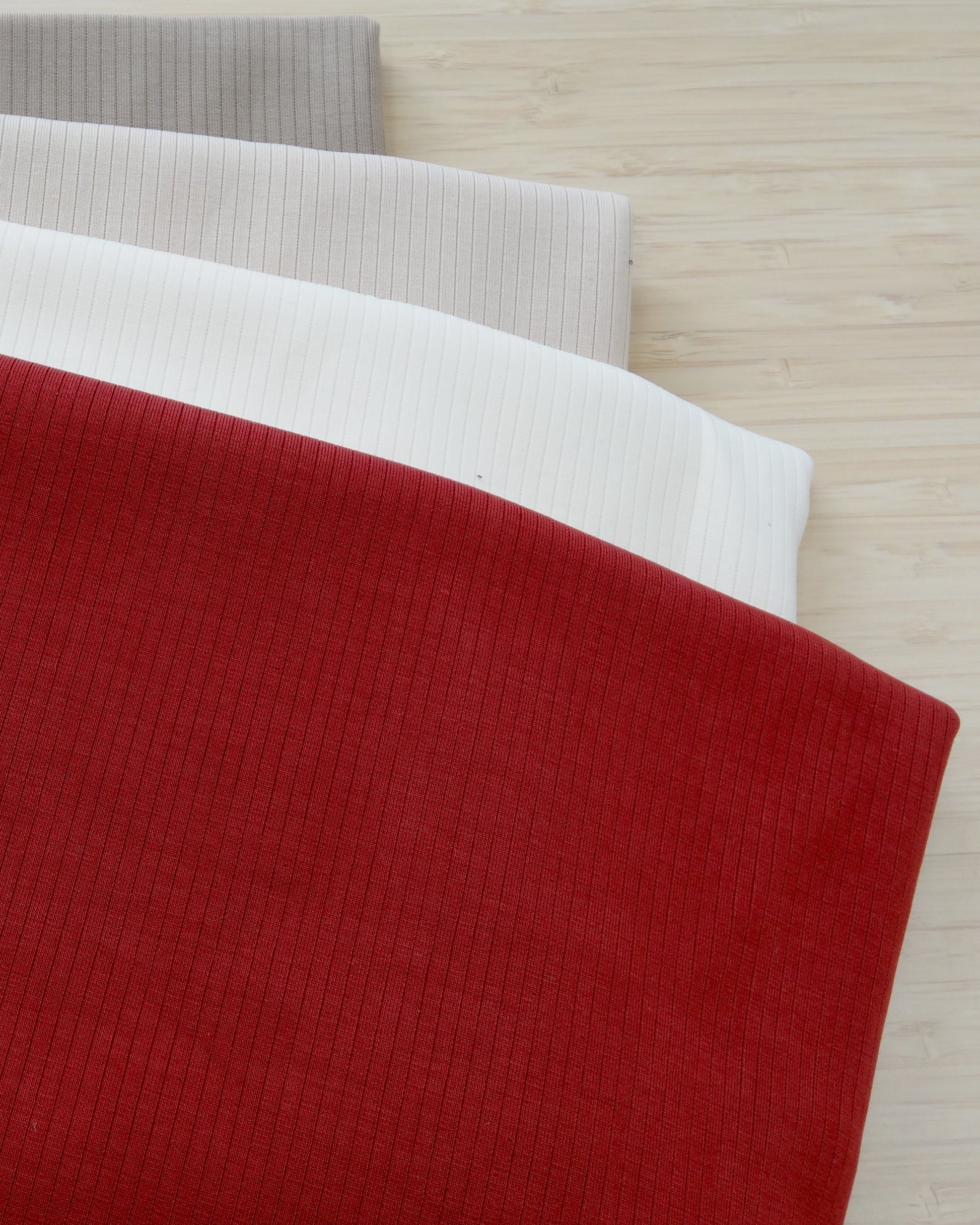 Four colours of ribbed knitted activewear fabric remnants folded and stacked on a wooden table