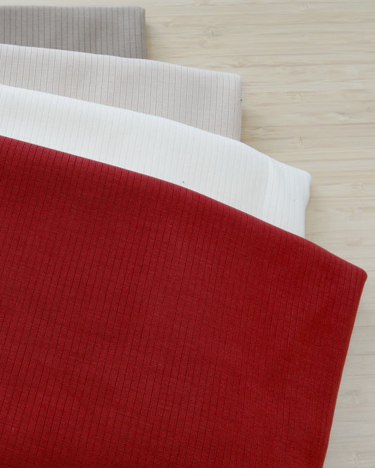 Four colours of ribbed knitted activewear fabric remnants folded and stacked on a wooden table