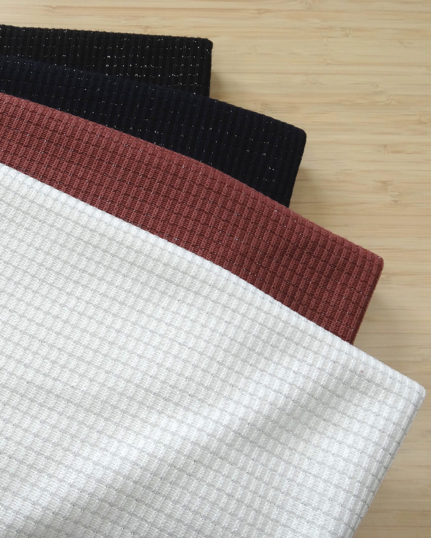 Four colours of ribbed knitted shimmery fabric remnants folded and stacked on a wooden table