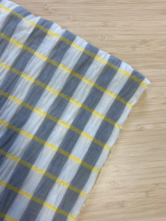 A white, grey, and yellow check style shirred voile fabric folded and photographed from above on a wooden table