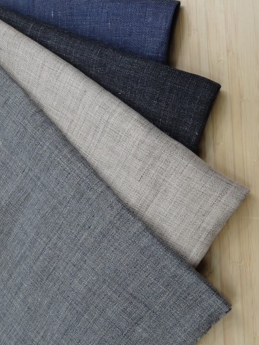 Four colours of Slubbed linen twill fabric remnants folded and stacked on a wooden table