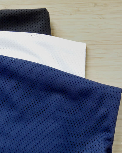 Three colours of mesh, navy, white and black folded and stacked on a wooden table
