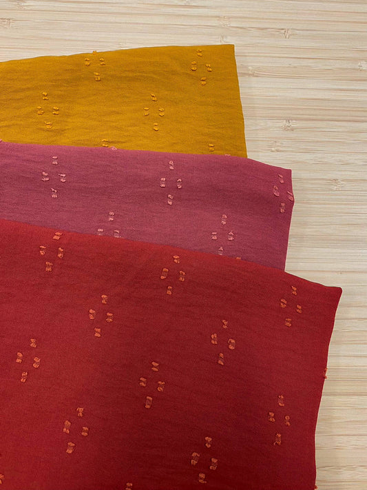 Photo of 3 different colours of Spot detail Jacquard fabric folded and stacked. photographed from above on a wooden table.
