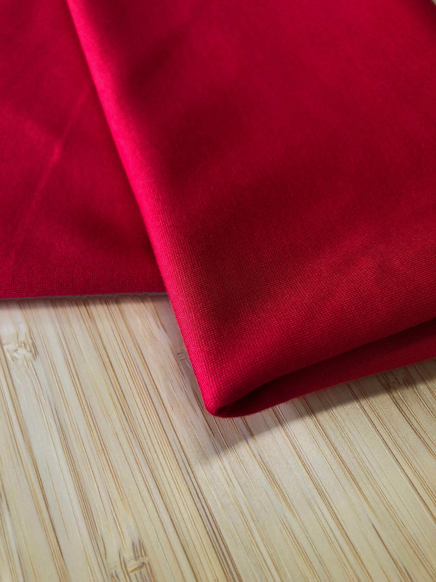 A red jersey fabric folded and photographed on a wooden table