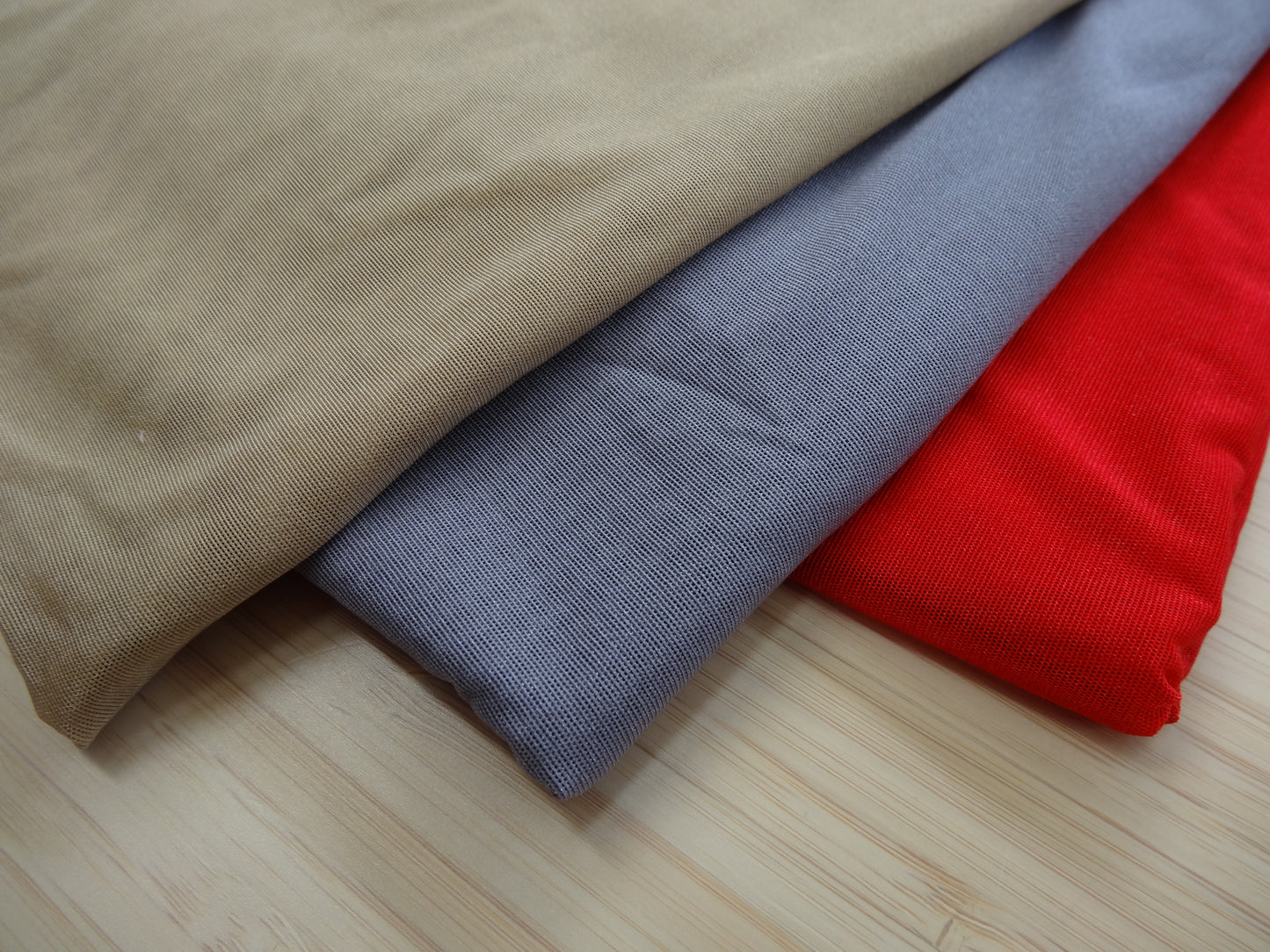 Photo of a stetchy mesh fabric in beige, grey, and red on a wooden table. photographed from above.