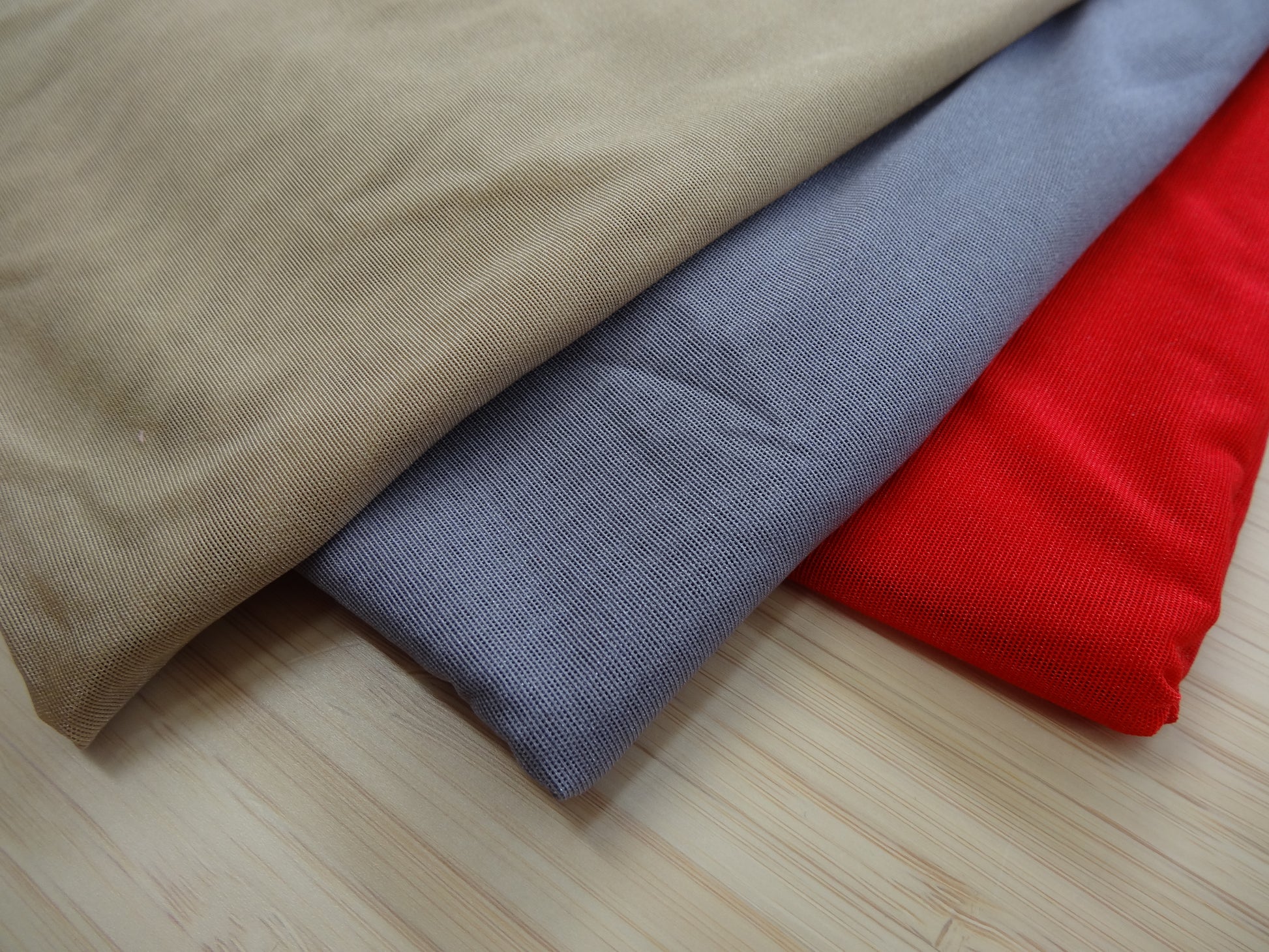 Photo of a stetchy mesh fabric in beige, grey, and red on a wooden table. photographed from above.