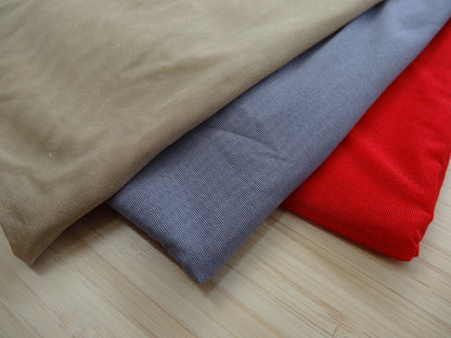 Photo of a stetchy mesh fabric in beige, grey, and red on a wooden table. photographed from above.
