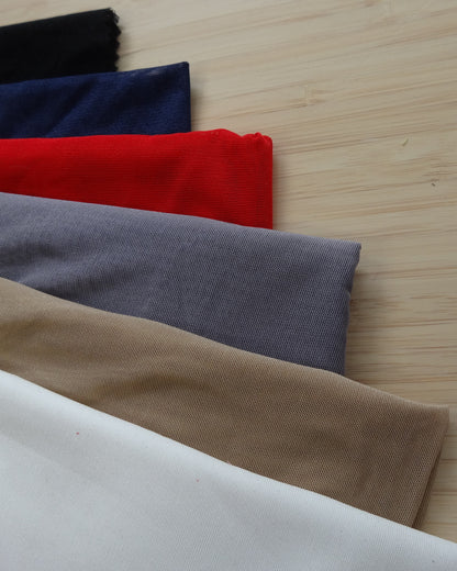 Photo of a stetchy mesh fabric in white, beige, grey, red, navy, and black on a wooden table. photographed from above.