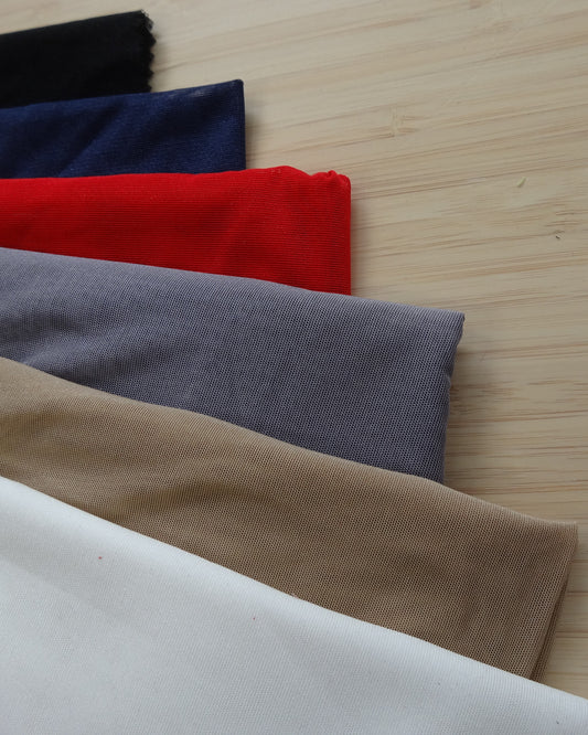 Photo of a stetchy mesh fabric in white, beige, grey, red, navy, and black on a wooden table. photographed from above.
